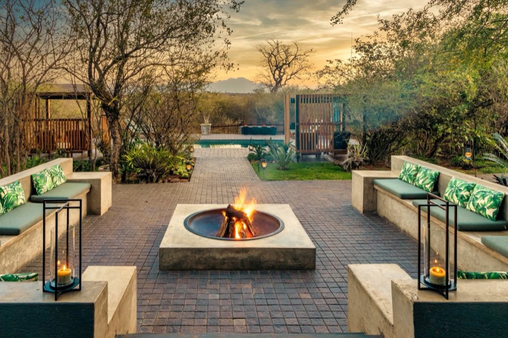 The boma at sunset — a fire lit in the round pit, lanterns along the built-in benches, and the pool and bush beyond.