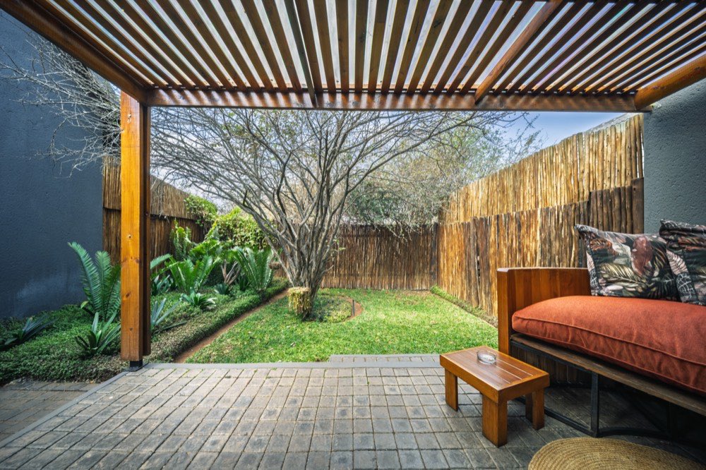 The Deluxe Garden Room's private walled garden seen from under a timber pergola, with a day bed and a marula tree.
