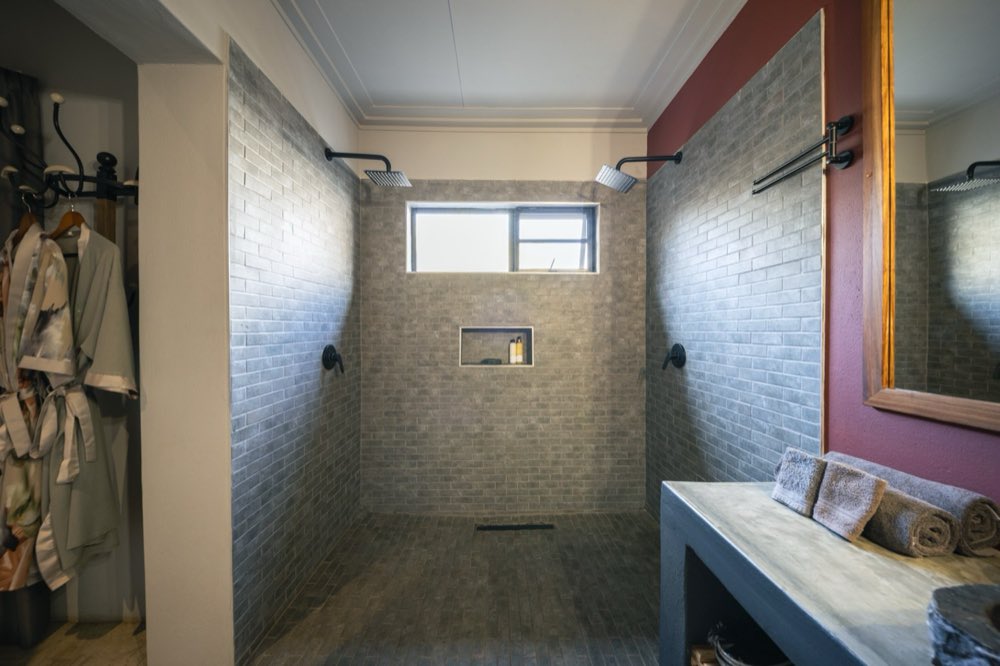 The Deluxe Garden Room's large double shower, tiled floor to ceiling in grey brick with twin rain heads.