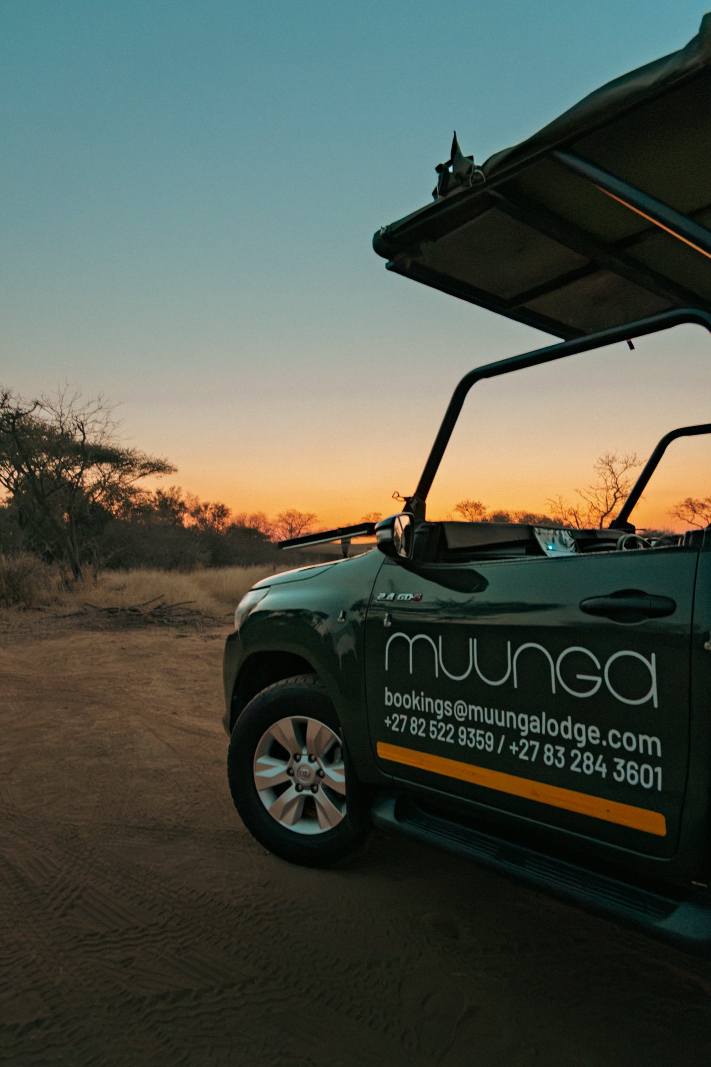 The Muunga game viewer parked on a sand track at sunset, the sky orange behind the treeline.