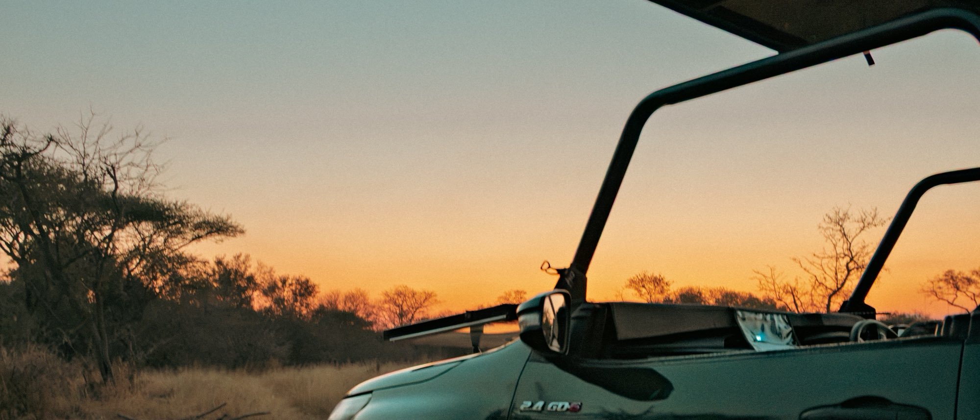 An open game viewer parked on a sand track at dusk, with bare winter trees and dry grass along an orange horizon.