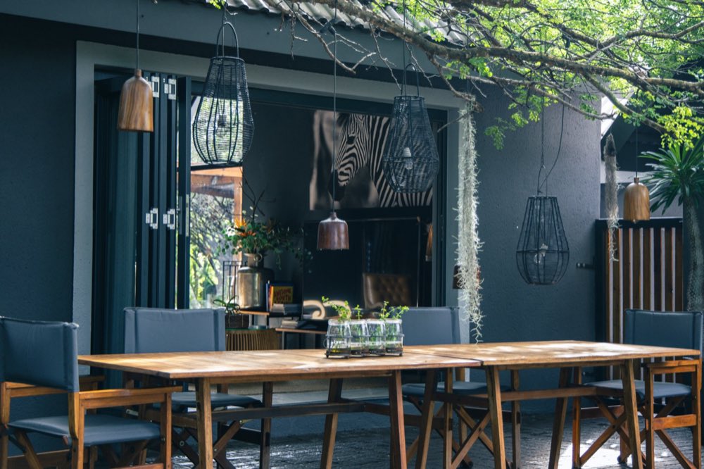 The long table outside the main lodge, woven pendant lanterns hanging above it and the doors folded open behind.