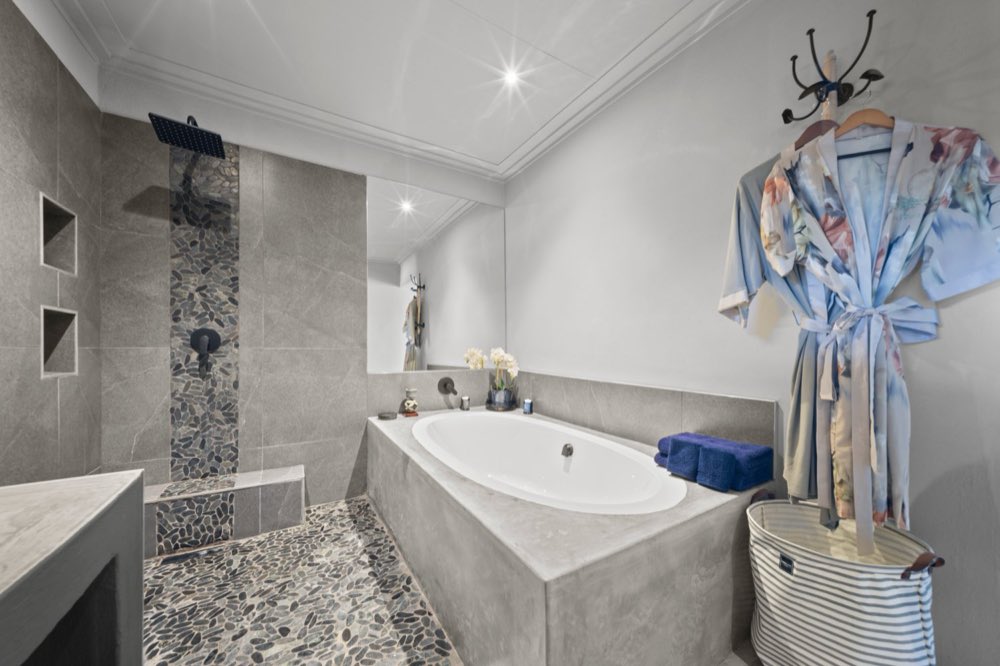 The Private Bush Cottage bathroom — a built-in bath beside a walk-in shower with a pebbled floor.