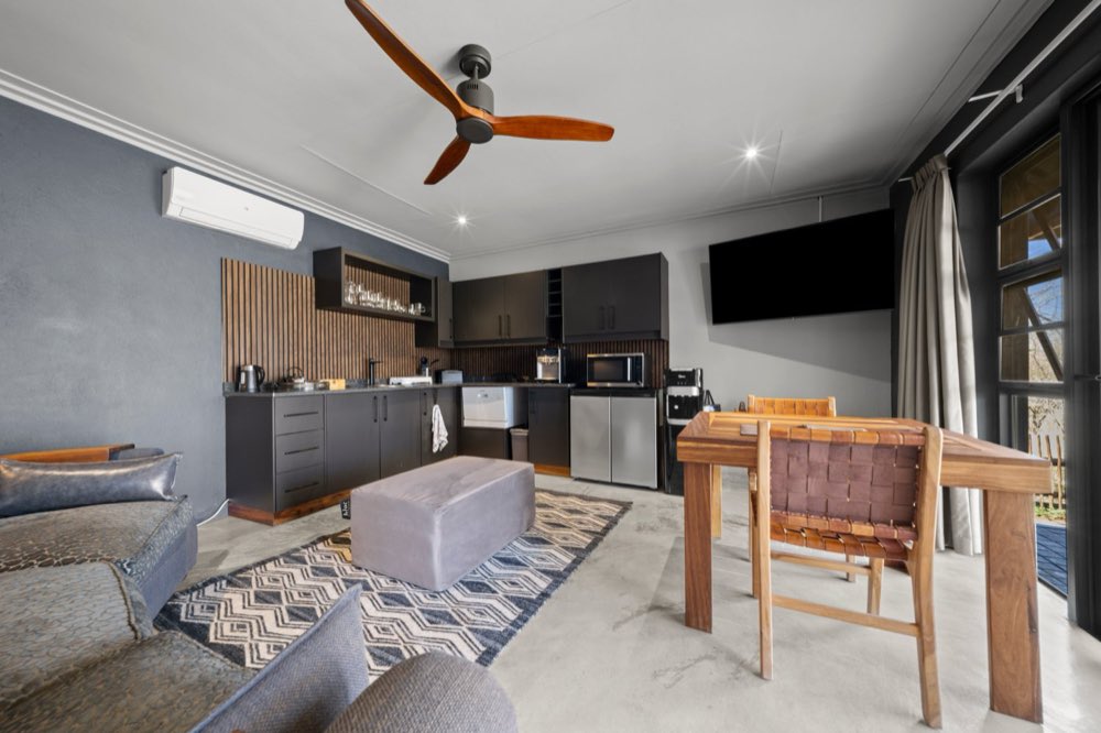 The Private Bush Cottage kitchenette and dining table, with a slatted timber splashback and a ceiling fan above.