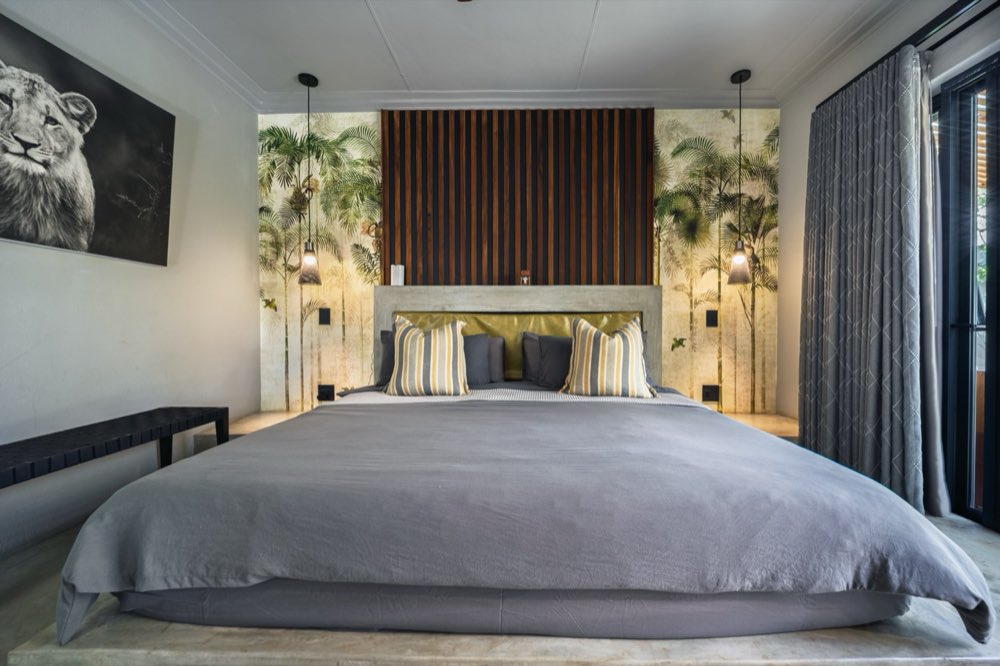 The Superior Bush Suite — a bed on a concrete plinth against a painted palm mural, with a gold headboard panel and a pendant light either side.